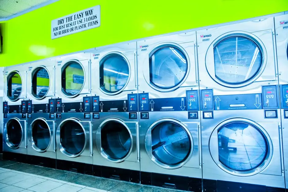 Bright modern laundromat with stainless steel industrial dryers and vibrant green wall.